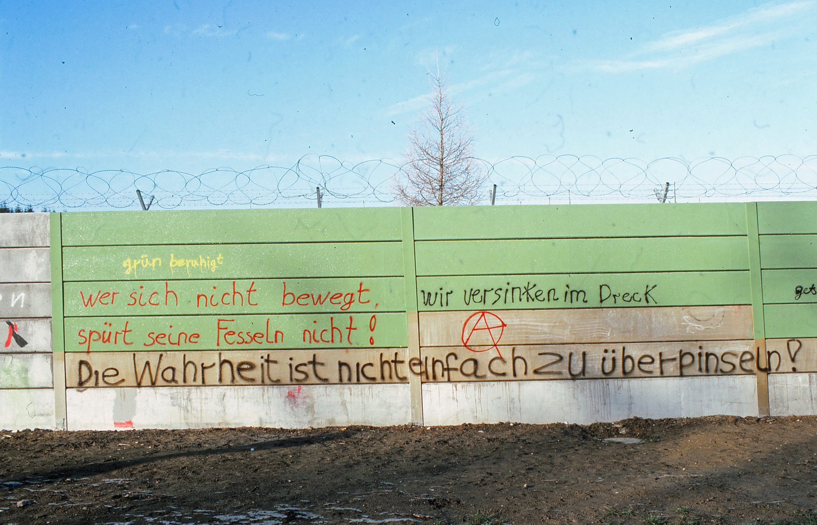 Frisch grün überstrichene Mauer, darauf erneut Parolen geschrieben